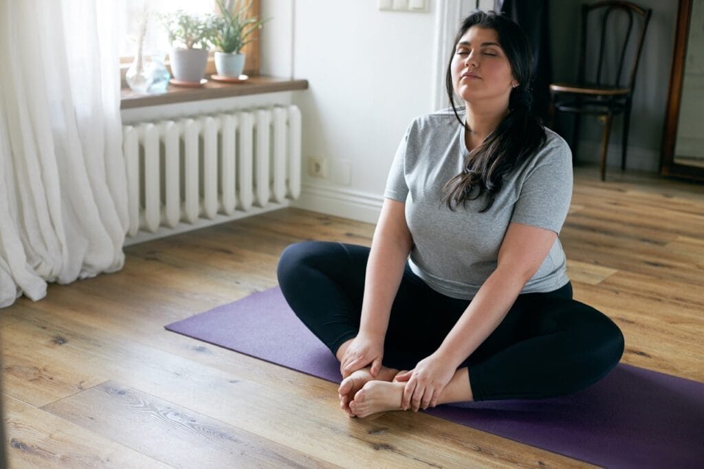 Woman in comfortable clothes practicing meditation on yoga mat at home